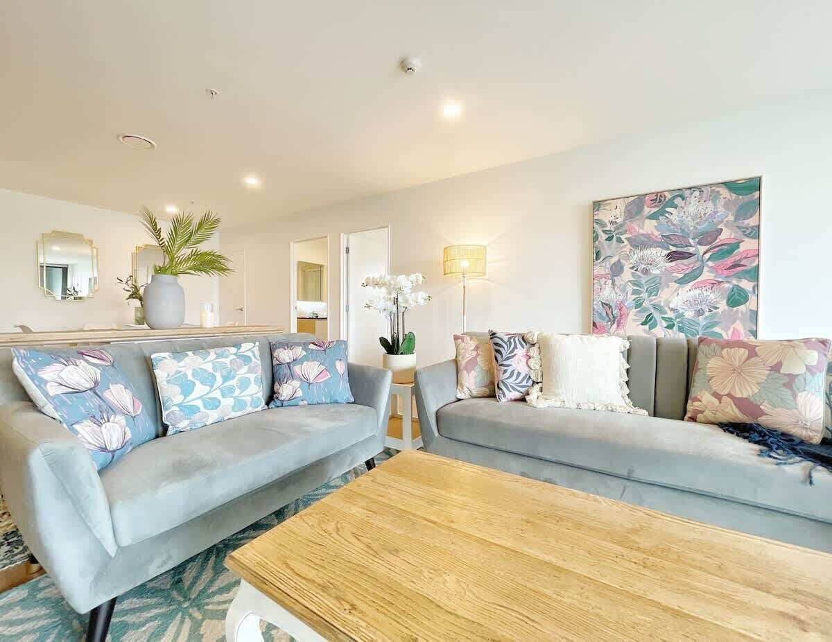Un salon moderne avec deux canapés gris, une table basse en bois et un tableau floral accroché au mur.