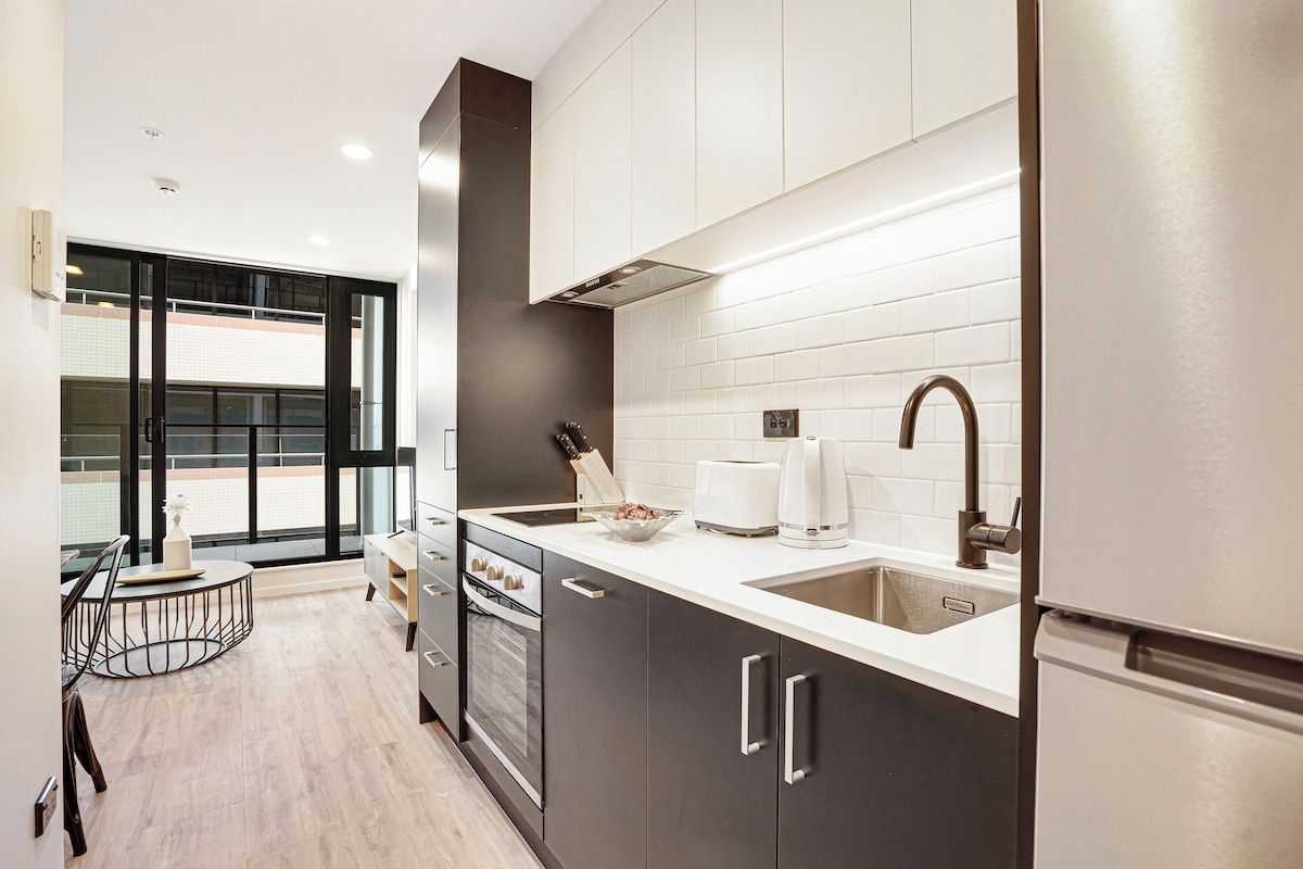 A modern kitchen with a large window, a built-in oven, and a refrigerator.