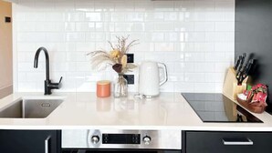 Eine moderne Küche mit weißen Schränken, einer Edelstahl-Spüle, einer Kaffeemaschine und einer Vase mit getrockneten Blumen.