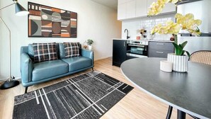 Ein modernes Wohnzimmer mit einem blauen Sofa, einem schwarz-weißen Teppich und einer Küchenzeile mit Herd, Schränken und gelben Orchideen.