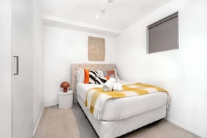 A modern bedroom with a large bed, a headboard, a bedside table, and a wall-mounted window.
