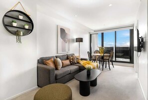 Ein modernes Wohnzimmer mit einem grauen Sofa, einem schwarzen Couchtisch und einem runden Regal mit Pflanzen.