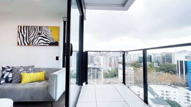 A modern apartment with a balcony, a grey sofa with yellow cushions, and a zebra-patterned artwork on the wall. - CBD Cozy Penthouse 1B Studio vs Pool Gym Sauna (Auckland)
