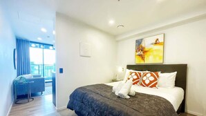 Ein Hotelzimmer mit einem großen Bett, einem Nachttisch, einem Gemälde an der Wand und Blick auf die Stadt durch das Fenster.