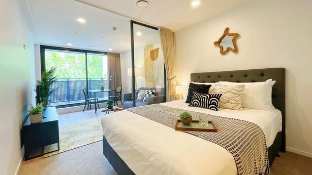 A modern bedroom with a large bed, a small desk, a balcony with a view, and a star-shaped wall decoration.