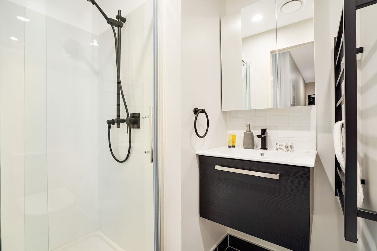 A modern bathroom with a glass shower enclosure, a black and white vanity, and a mirror above the sink.