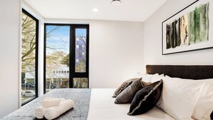 Ein modernes Hotelzimmer mit einem großen Bett, Blick auf die Stadt durch ein großes Fenster und einem Gemälde an der Wand.