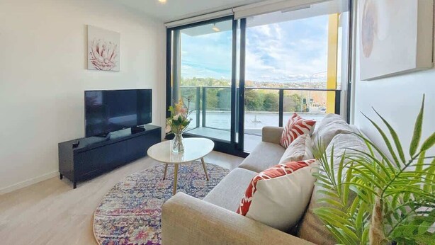 Uma sala de estar moderna com uma televisão grande, um sofá, uma mesa de centro e vista pela janela.