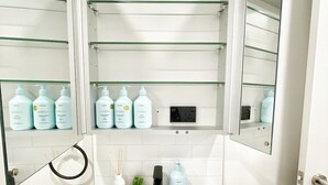 Une salle de bain moderne avec un lavabo blanc, des armoires à miroir et des étagères où sont rangés les produits de toilette.