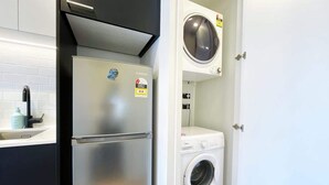 Une cuisine compacte équipée d’un réfrigérateur en acier inoxydable, d’un lave-linge et d’un évier avec un robinet.