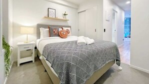 A modern bedroom with a bed, bedside table, and a nightstand. There is a hallway leading to another room.