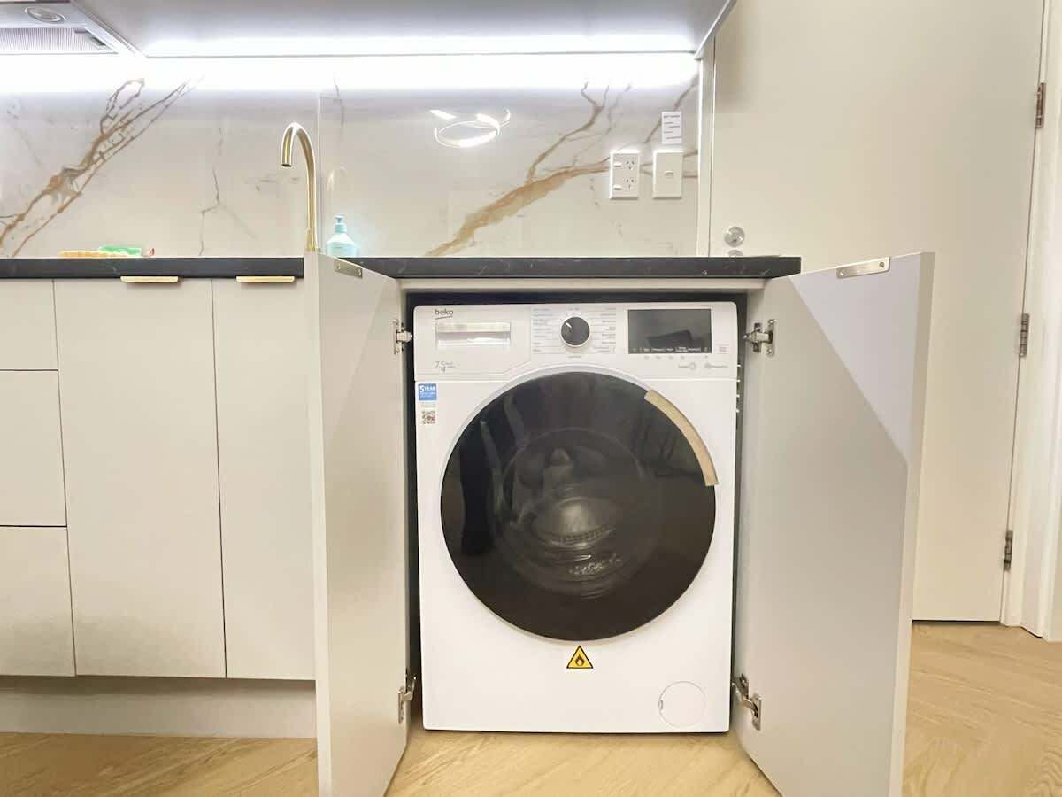 Ein kompakter, moderner Waschraum mit einer Waschmaschine, einer Bedienkonsole und einem Sicherheitshinweis.