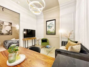 A modern living room with a flat-screen TV, a green armchair, a sofa with cushions, a glass coffee table, and a wooden dining table. - Stylish Chic Stunning 1BR Gem in Central Queen St (Auckland)