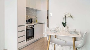 A modern kitchen with white cabinets, a built-in oven, and a dining area with a white table and chairs. - Stunning & Bright Studio in Central -Swimming Pool (Auckland)