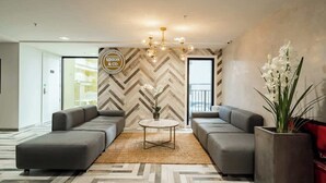 A modern hotel lobby with a herringbone-patterned wall, a central round coffee table, two grey sofas, and a decorative chandelier. - Stunning & Bright Studio in Central -Swimming Pool (Auckland)