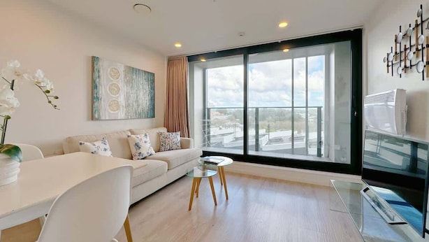 A modern living room with a sofa, a dining table, and a large window with a view. - Stunning & Bright Studio in Central -Swimming Pool (Auckland)