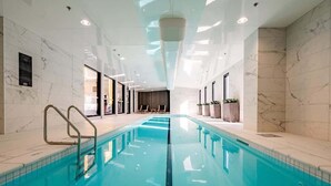 An indoor swimming pool with clear water, surrounded by marble walls and a modern ceiling design. - Central Stylish Comfy Studio with Swimming Pool (Auckland)