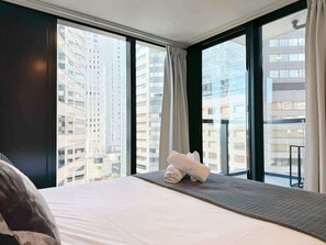 A hotel room with a large bed, a view of tall buildings, and a window with curtains. - Modern 2 Bedroom Beside SkyTower,Queen St vs Pool (Auckland)