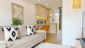 Ein modernes Wohnzimmer mit einer Couch, einem Esstisch und Stühlen. Im Hintergrund ist eine Küche zu sehen.