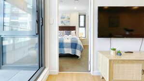 Ein modernes Hotelzimmer mit einem großen Bett, einem an der Wand befestigten Fernseher und einer Holzkommode mit einer Pflanze.