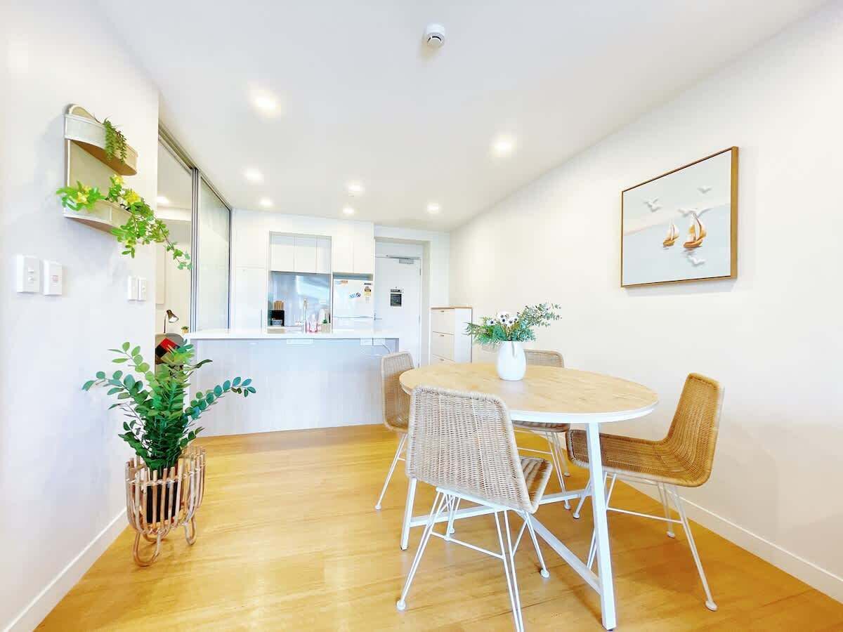 A modern dining area with a round table and wicker chairs, a potted plant, and a framed picture on the wall.