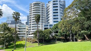 A modern building complex with multiple high-rise structures, surrounded by well-maintained green lawns and palm trees. - Parkside Elegance 1BR on Queen St vs Pool & Gym (Auckland)