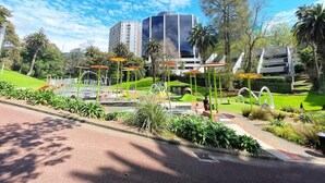 A park with playground equipment, a building in the background, and a clear sky. - Parkside Elegance 1BR on Queen St vs Pool & Gym (Auckland)