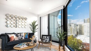 A modern living room with a black sofa, a patterned armchair, a coffee table, and a large window with a city view.