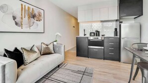 A modern kitchen with white cabinets, a stainless steel refrigerator, and a dining area with a table and chairs. - CBD High Level Stylish 1B Studio vs Pool Gym Sauna (Auckland)