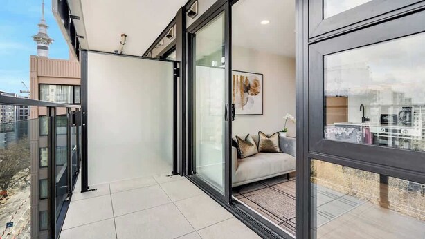A modern apartment with a balcony, large sliding glass doors, a sofa with cushions, and a city view. - CBD High Level Stylish 1B Studio vs Pool Gym Sauna (Auckland)