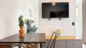Ett modernt vardagsrum med en platt-TV som är monterad på väggen, ett matbord i trä och en grå soffa.