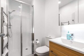 A modern bathroom with a glass-enclosed shower, a white toilet, a wooden vanity with a sink, and a mirror above the vanity.