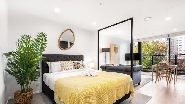 Een moderne slaapkamer met een groot bed, een potplant, een spiegel en uitzicht op het omliggende landschap.