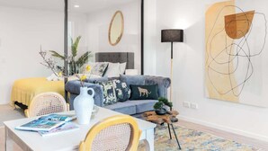 Een moderne woonkamer met een grijze bank, een witte salontafel en een groot abstract schilderij aan de muur.