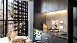Een moderne keuken met donkerhouten kasten, een glazen aanrecht en een inbouwoven. Op het aanrecht staat een vaas met gedroogde bloemen.