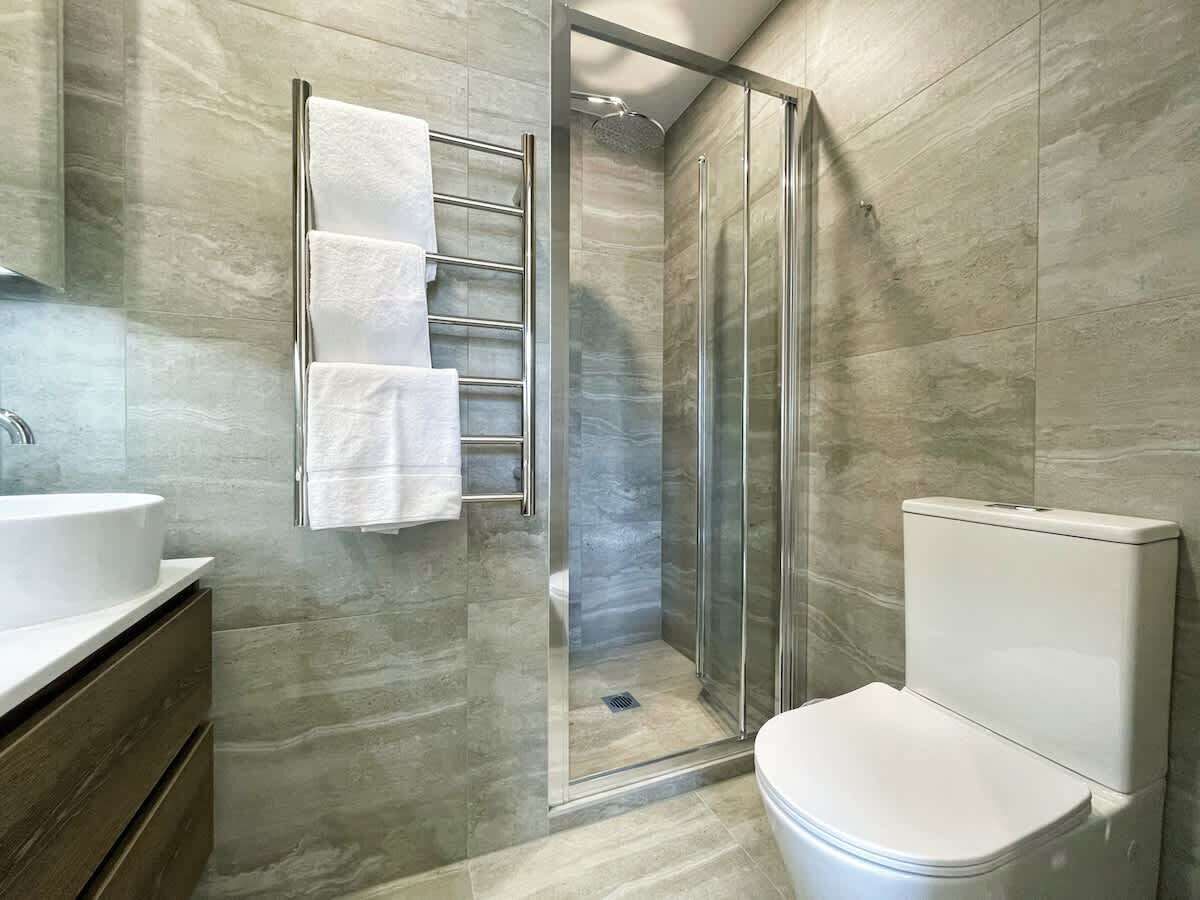 Een moderne badkamer met een douchecabine van glas, een wit toilet en een wastafelmeubel met een wastafel.