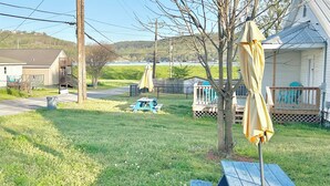 A grassy backyard with a picnic table and umbrellas, a wooden deck, and a playground structure. - Charming 2-bedroom cottage, sleeps 2-4, with WiFi & AC in adorable Guntersville (Guntersville)