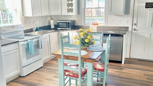 A kitchen with white cabinets, a wooden dining table with chairs, a chandelier, and a view through the window. - Charming 2-bedroom cottage, sleeps 2-4, with WiFi & AC in adorable Guntersville (Guntersville)