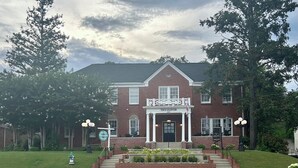 A brick building with a central entrance, a porch, and a sign reading "The Glover". - Charming 2-bedroom cottage, sleeps 2-4, with WiFi & AC in adorable Guntersville (Guntersville)