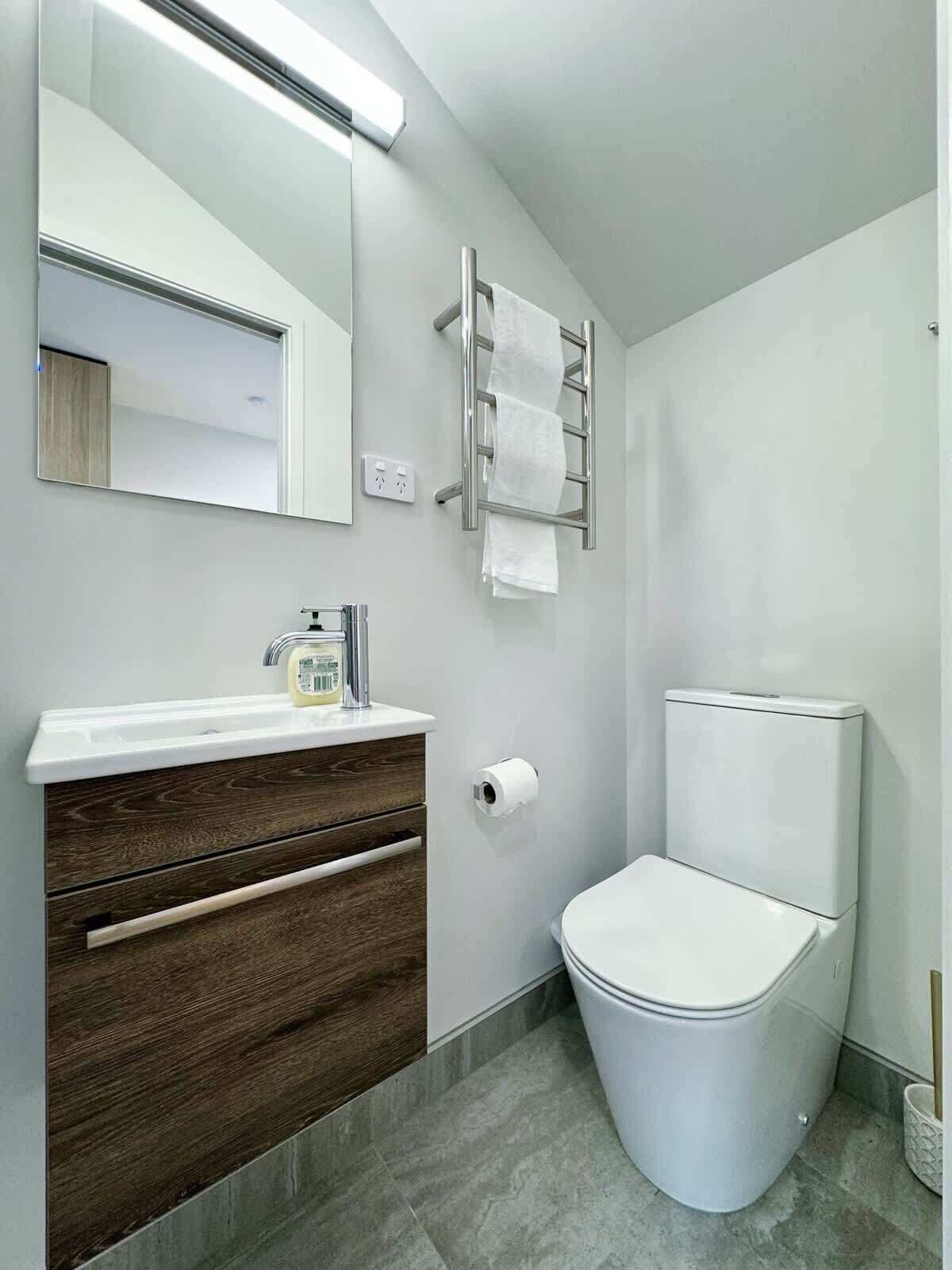 Une salle de bain moderne avec un lavabo blanc, un meuble-lavabo en bois foncé, des toilettes et un porte-serviettes.
