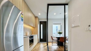 A modern kitchen with a stainless steel refrigerator, wooden cabinets, and a dining area with a table and chairs.