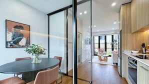 A modern kitchen with wooden cabinets, a dining area with a round table and chairs, and a glass partition separating the two spaces.