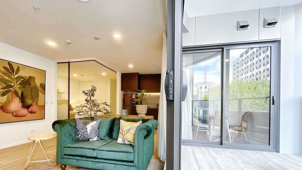 A modern living room with a green sofa, a wooden coffee table, and a large painting on the wall. - Parkside Living Unique1B Apt in CBD vs Pool & Gym (Auckland)