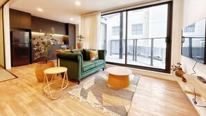 A modern living room with a green sofa, a round coffee table, and a large window offering a view of buildings. - Parkside Living Unique1B Apt in CBD vs Pool & Gym (Auckland)