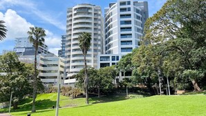 A modern building complex with multiple floors, surrounded by lush greenery and palm trees. - Parkside Living Unique1B Apt in CBD vs Pool & Gym (Auckland)