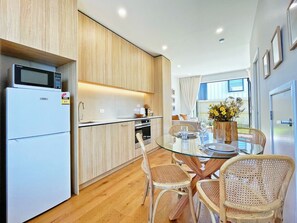 Una cocina moderna con armarios de madera, un refrigerador blanco y una zona de comedor con sillas de mimbre y una mesa de vidrio.