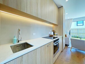 Una cocina moderna con horno empotrado, un lavamanos y una zona de comedor con una silla blanca.