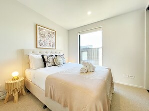 A hotel room with a bed, a bedside table with a lamp, a window, and a wall-mounted artwork.