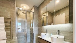 Ein modernes Badezimmer mit einer Duschkabine, zwei Waschbecken und einem großen Spiegel.