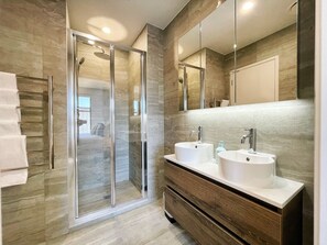 A modern bathroom with a glass-enclosed shower, two sinks, and a large mirror.